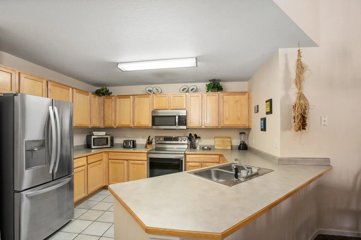 A bright and functional kitchen with a stainless steel refrigerator, kitchen island, wooden cabinetry, and a central sink. The ample counter space and modern appliances are ideal for cooking and socializing.