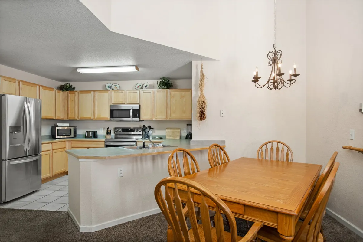This image showcases a welcoming dining table set next to a kitchen island with stainless steel appliances, illuminated by a chandelier. The layout highlights the easy flow between the kitchen and dining area, making it ideal for family meals and group gatherings.