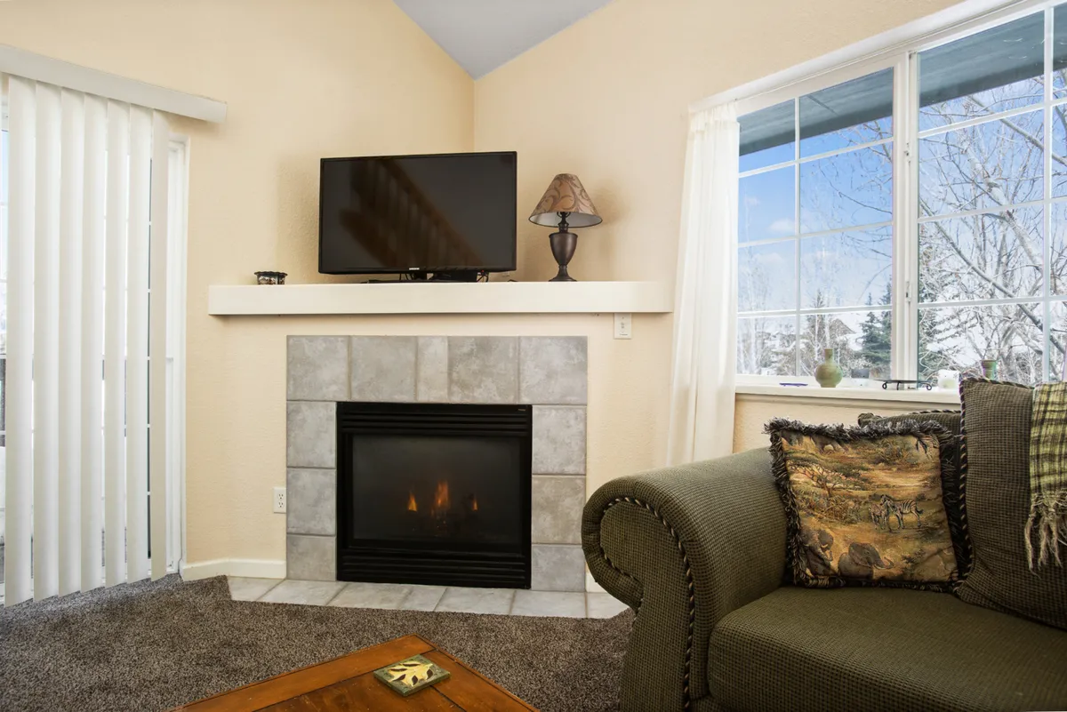 A cozy living room featuring a fireplace, TV, comfortable couch, and a window offering a glimpse of the outdoors. The room feels inviting and warm, hinting at relaxation after a day spent outside.
