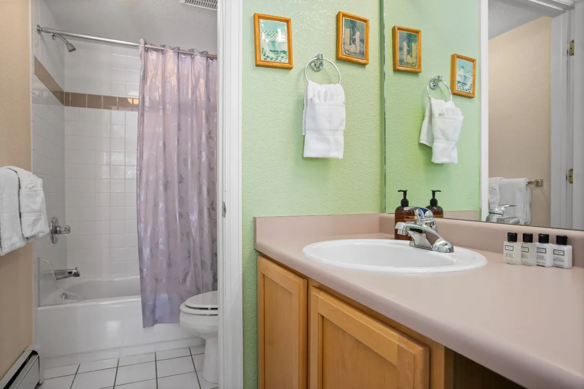 A bright, functional bathroom featuring a sink area, large mirror, shower curtain, and cheerful artwork. The space is designed for convenience and comfort.