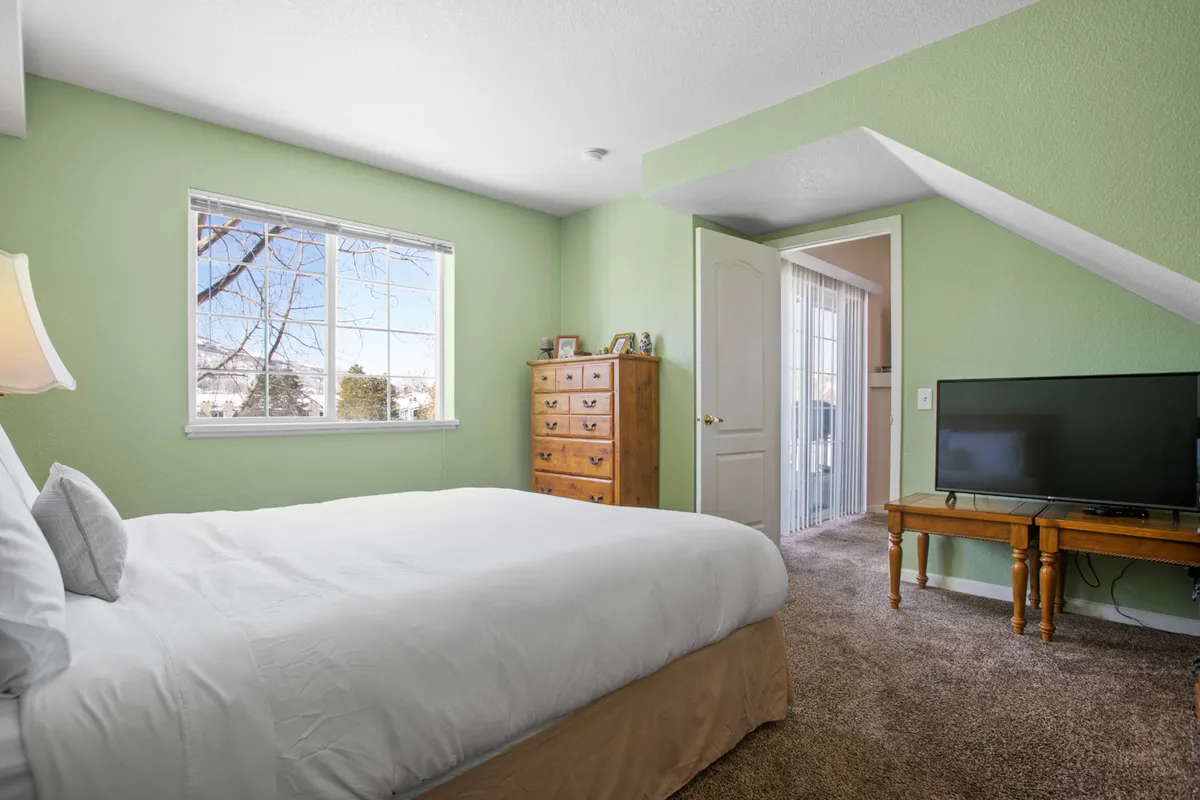 A comfortable bedroom featuring a plush bed, large window, dresser, TV, and soft lighting, offering a cozy retreat for evenings spent in. The room looks inviting for relaxing after a night out or streaming a movie by the fire, as referenced in the section.