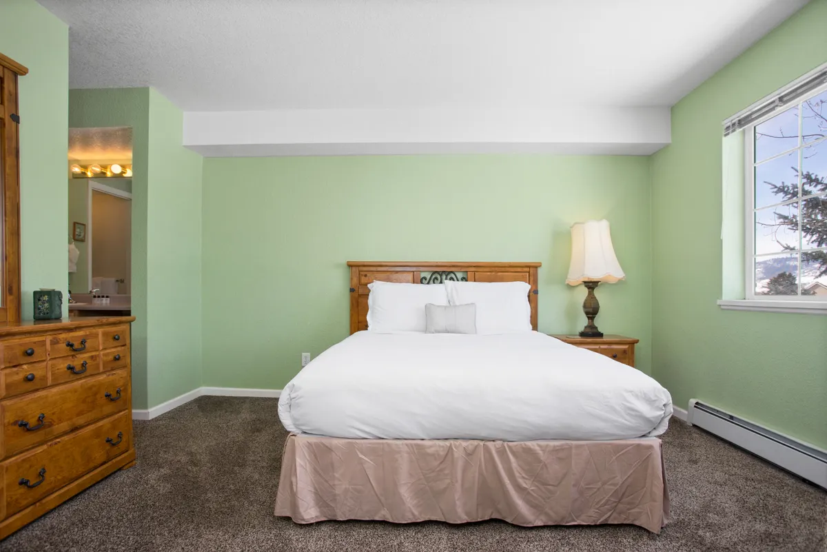 A tranquil bedroom with a neatly made bed, nightstand, dresser, and window letting in natural light. The serene atmosphere is perfect for restful nights or taking a quiet break from work or adventures. The neutral decor and ample light make it ideal for long-term comfort.
