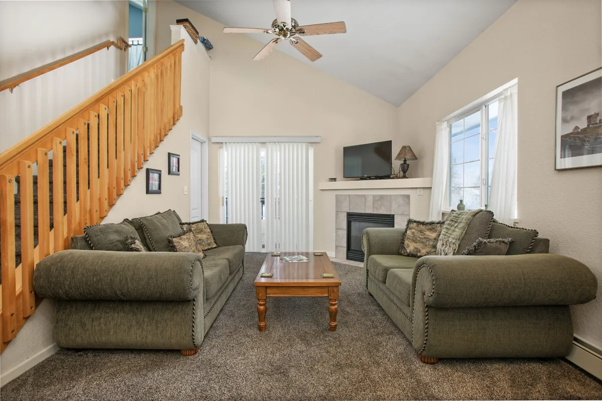 This image showcases a cozy living room featuring comfortable sofas arranged around a coffee table and a welcoming fireplace, with a TV and an open staircase in the background. The space feels inviting for relaxing after a day of outdoor activities and encourages socializing and gathering.